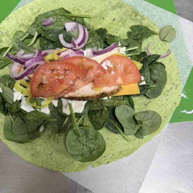 A spinach wrap layered with greens, tomato, onion, cheese and filling